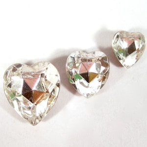 Peut inclure: Trois strass en verre transparent en forme de cœur de différentes tailles. Les strass ont un design facetté et une finition réfléchissante.