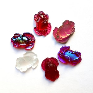 Op de afbeelding: Zes regenboogkleurige glazen bedels in de vorm van een roos, een vis, een krab en drie andere abstracte vormen. De bedels zijn in tinten rood, roze, blauw en wit.