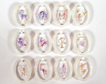 Puede incluir: Doce amuletos ovalados blancos iridiscentes con símbolos del zodíaco. Los símbolos son: Aries, Tauro, Géminis, Cáncer, Leo, Virgo, Libra, Escorpio, Sagitario, Capricornio, Acuario y Piscis.