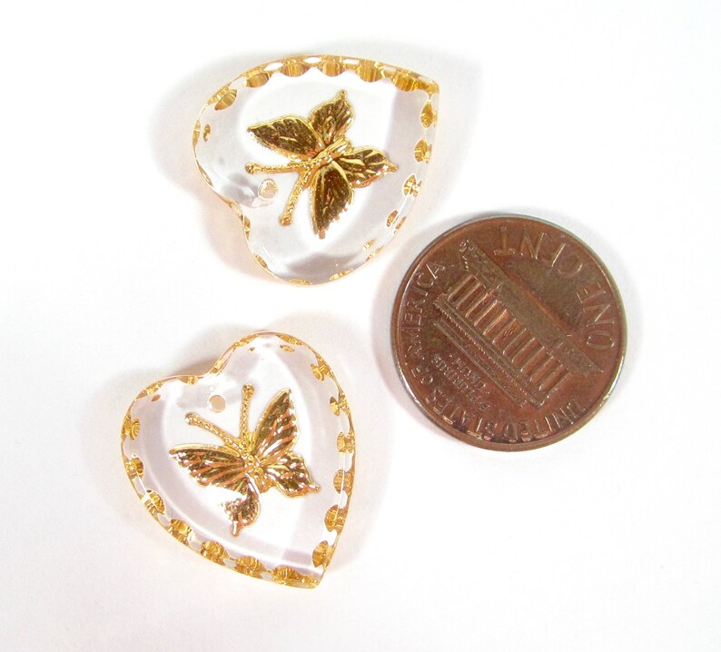 Puede incluir: Tres colgantes transparentes en forma de coraz&oacute;n con dise&ntilde;os de mariposas doradas y adornos dorados. Se incluye una moneda para comparar el tama&ntilde;o. Los colgantes tienen un peque&ntilde;o agujero en la parte superior para ensartar.