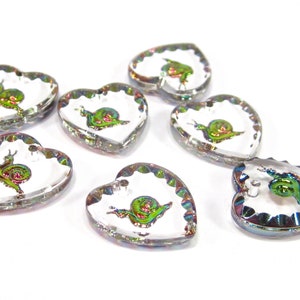 May include: Seven iridescent heart-shaped glass charms with a snail design. Each charm has a scalloped edge and a clear background.