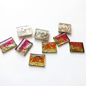 May include: A collection of small, rectangular, decorative tiles with various designs. Some tiles feature palm trees and flamingos in gold and orange, while others have floral or abstract patterns in silver and red.