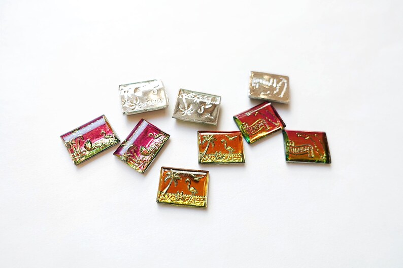 May include: A collection of small, rectangular, decorative tiles with various designs. Some tiles feature palm trees and flamingos in gold and orange, while others have floral or abstract patterns in silver and red.