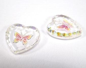 May include: Two clear, heart-shaped glass ornaments. Each ornament features a colorful butterfly design with red, yellow, and orange wings. The edges of the hearts have a faceted, iridescent finish, creating a shimmering effect. These decorative ornaments are ideal for adding a touch of whimsy.