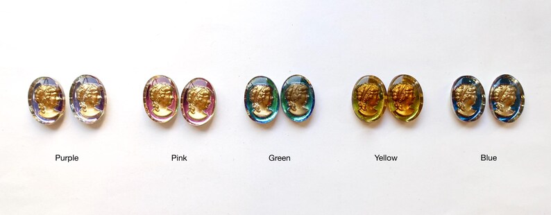 K&ouml;nnte beinhalten: F&uuml;nf Paare ovaler Ohrringe aus Glas mit goldfarbenen Kameen-Designs. Die Ohrringe sind in einer Reihe angeordnet, wobei jedes Paar eine andere Farbe hat: lila, rosa, gr&uuml;n, gelb und blau.