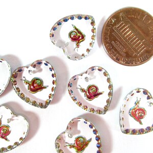 May include: Eight iridescent heart-shaped buttons with a snail design. The buttons are approximately the size of a UK penny.