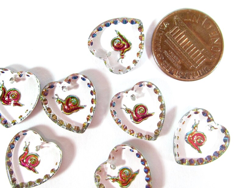 May include: Eight iridescent heart-shaped buttons with a snail design. The buttons are approximately the size of a UK penny.