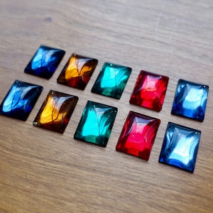 Peut inclure: Dix petits carreaux de verre rectangulaires avec une variété de couleurs et de motifs. Les carreaux sont disposés en deux rangées de cinq. Les couleurs comprennent le bleu, le vert, le rouge et l'orange.