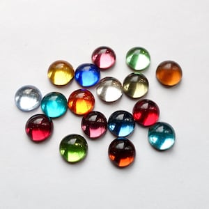 Op de afbeelding: Assortiment van ronde, kleurrijke glazen cabochons. De cabochons zijn in verschillende tinten rood, blauw, groen, geel en helder.