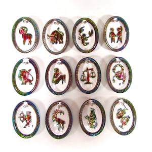 May include: Twelve oval-shaped charms with iridescent borders, each featuring a different zodiac sign in gold and red. The charms are arranged in three rows of four.