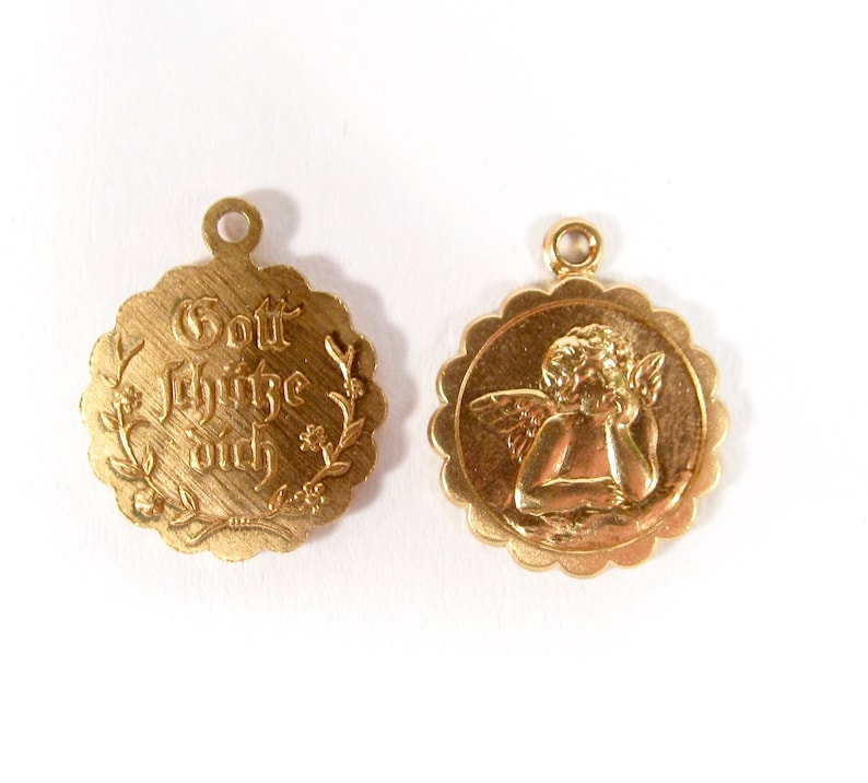 May include: Two gold-colored pendants. One pendant features a cherub with wings, the other pendant has the text "Gott sch&uuml;tze dich" in a decorative font.