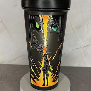 May include: Black shaker bottle with a graphic of a character from the anime Attack on Titan. The character has green eyes and is surrounded by yellow and orange flames.