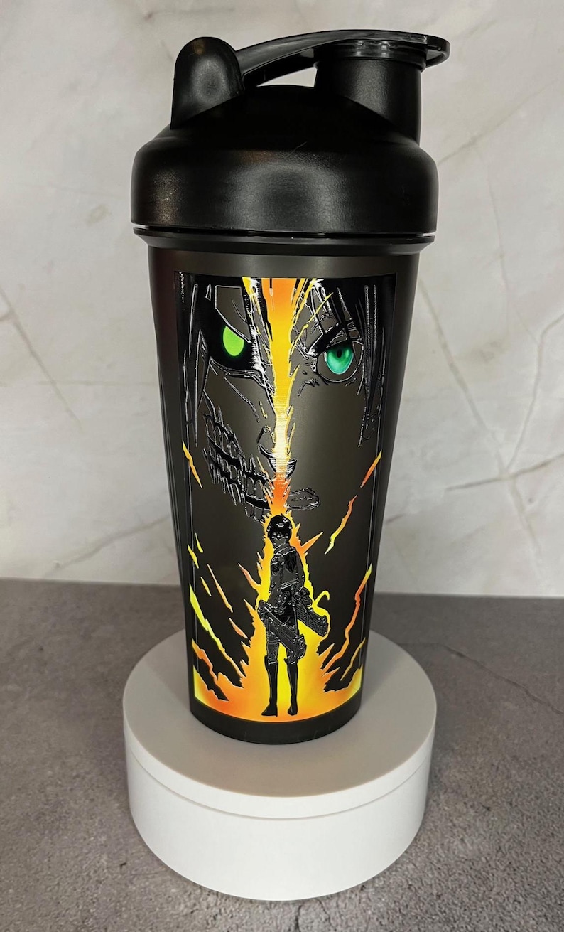 May include: Black shaker bottle with a graphic of a character from the anime Attack on Titan. The character has green eyes and is surrounded by yellow and orange flames.