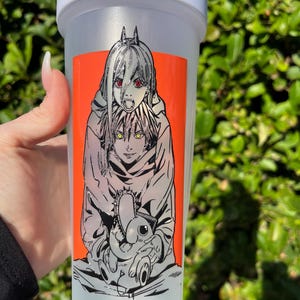 Pu&ograve; includere: Una bottiglia shaker in plastica trasparente con coperchio bianco. La bottiglia presenta un adesivo arancione vibrante con un'illustrazione in stile manga di due personaggi. Un personaggio ha gli occhi rossi e l'altro gli occhi gialli. L'illustrazione &egrave; delineata in nero.