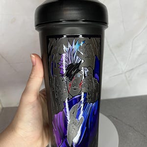May include: Black shaker bottle with a graphic of an anime character with white hair and a purple and blue outfit. The character is surrounded by a black and white background.