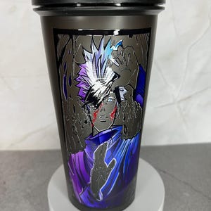 May include: Black shaker bottle with a graphic of a character with white hair and a purple and blue outfit. The character has a red mark on their face.