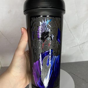 May include: Black shaker bottle with a graphic of a character with white hair and a purple and blue outfit. The character has a red mark on their face.