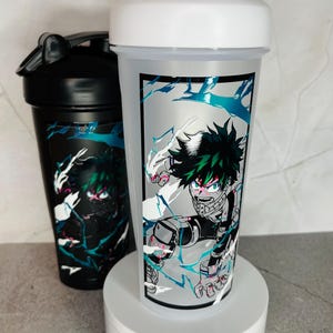 May include: Two white and black shaker bottles with a green and black anime character design. The character is surrounded by blue and white lightning bolts.