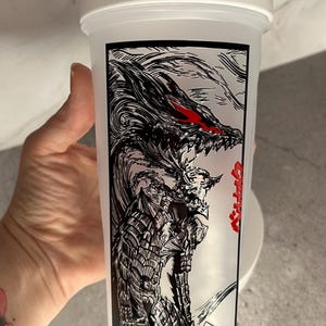 May include: White plastic shaker bottle with a black and red graphic of a dragon-like creature. The design features intricate details and the text in Japanese. The bottle has a white lid with a handle.