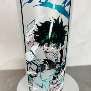May include: A white tumbler with a black border around a graphic of a green-haired anime character with a white and blue background. The character is in a fighting pose with their fist raised.