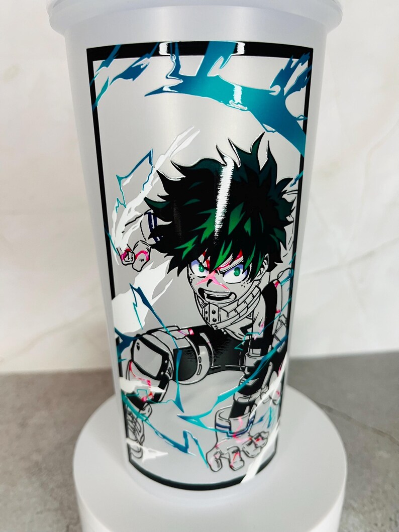 May include: A white tumbler with a black border around a graphic of a green-haired anime character with a white and blue background. The character is in a fighting pose with their fist raised.