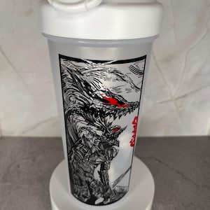 May include: A white plastic shaker bottle with a black and red graphic of a dragon-like creature. The bottle has a white lid with a flip-top closure and a carrying handle. The graphic is detailed and covers a large portion of the bottle.