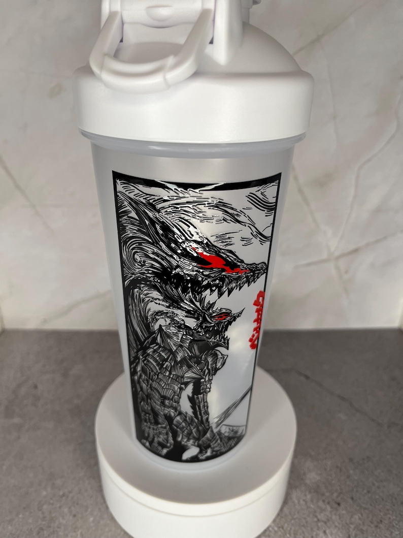 May include: A white plastic shaker bottle with a black and red graphic of a dragon-like creature. The bottle has a white lid with a flip-top closure and a carrying handle. The graphic is detailed and covers a large portion of the bottle.