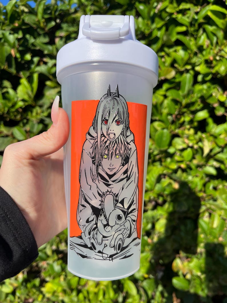 Pu&ograve; includere: Una bottiglia shaker in plastica trasparente con coperchio bianco. La bottiglia presenta una vivace grafica rettangolare arancione con un'illustrazione in stile manga di due personaggi. Uno ha i capelli argentati e gli occhi rossi.