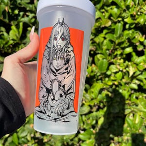 Pu&ograve; includere: Una bottiglia shaker in plastica trasparente con coperchio bianco e chiusura a ribalta. La bottiglia presenta una vivace grafica rettangolare arancione con un'illustrazione in bianco e nero in stile anime di due personaggi. Lo sfondo &egrave; verde sfocato.