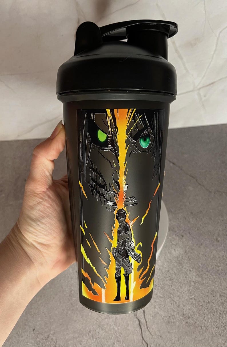 May include: Black shaker bottle with a graphic of a character from the anime Attack on Titan. The character has green eyes and is surrounded by yellow and orange flames.