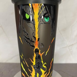 May include: Black shaker bottle with a graphic of a character from the anime Attack on Titan. The character is depicted with a fierce expression and glowing yellow and orange energy behind them.