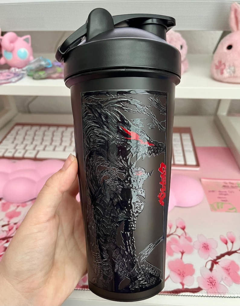 May include: Black water bottle with a dragon graphic. The bottle has a black lid and a flip-top opening. The dragon design is detailed with red eyes and Japanese text. The bottle is held in a hand.