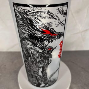 May include: A clear plastic tumbler with a white lid. The tumbler features a black and white illustration of a monster with red eyes and Japanese text. The design wraps around the cup.