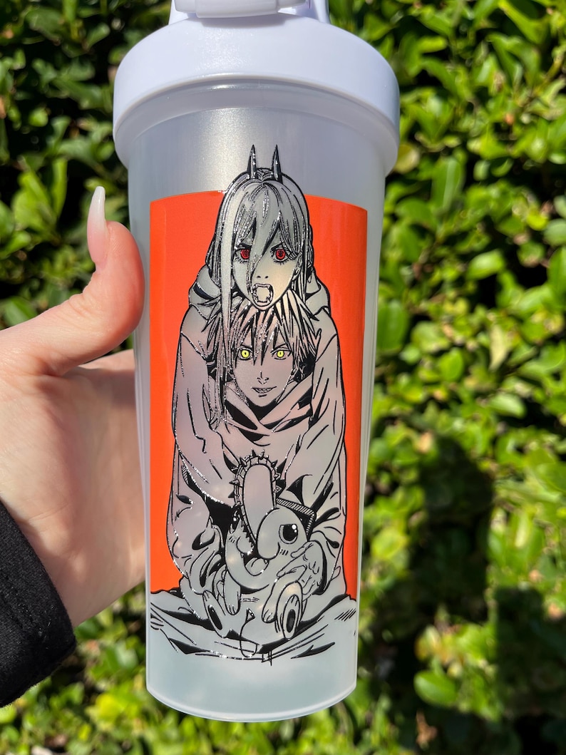 Pu&ograve; includere: Una bottiglia shaker in plastica trasparente con coperchio bianco. La bottiglia presenta un vivace adesivo rettangolare arancione con un'illustrazione in bianco e nero in stile anime di due personaggi. Un personaggio ha gli occhi rossi e l'altro gli occhi gialli.