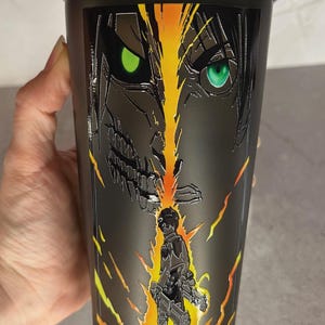 May include: Black shaker bottle with a graphic of a character from the anime Attack on Titan. The character is standing in front of a giant, menacing figure with glowing green eyes.