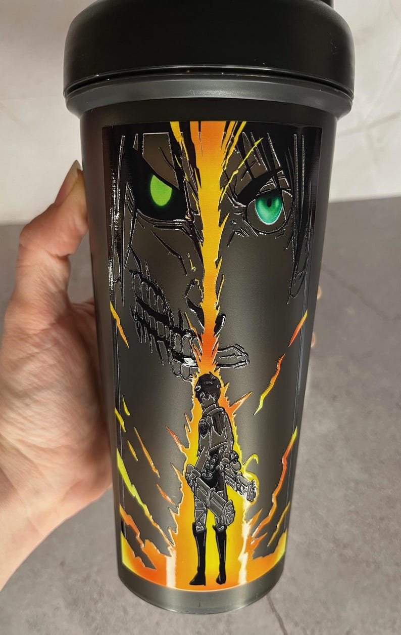 May include: Black shaker bottle with a graphic of a character from the anime Attack on Titan. The character is standing in front of a giant, menacing figure with glowing green eyes.
