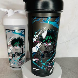 May include: Two black and white shaker bottles with a green and white anime character design. The character is in a fighting pose with a black mask and green hair.