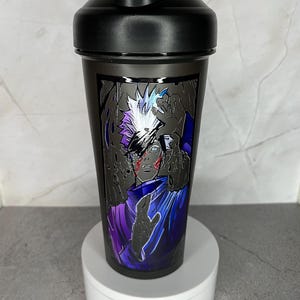 May include: Black shaker bottle with a graphic of a white-haired anime character with a purple and blue outfit. The character has a red mark on their face and is surrounded by black hands.