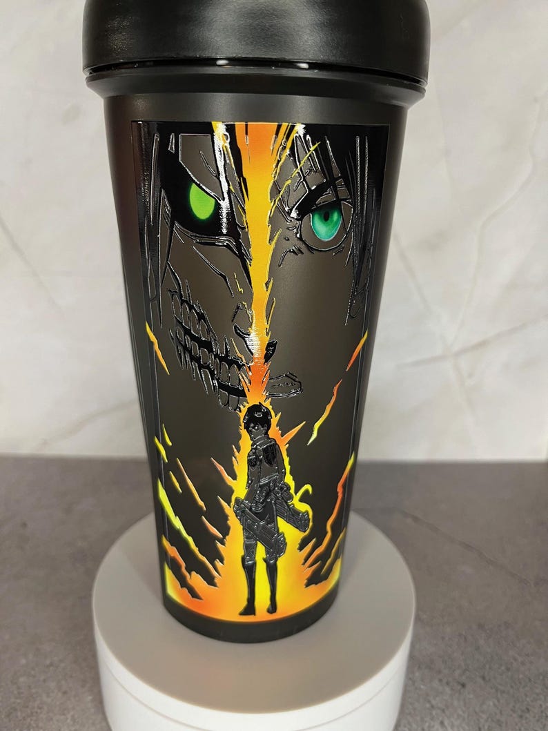 May include: Black shaker bottle with a graphic of a character from the anime Attack on Titan. The character is surrounded by flames and has green eyes.