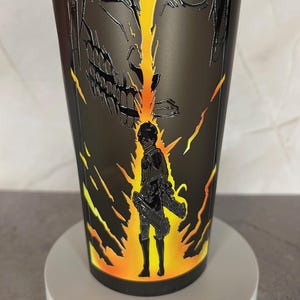May include: Black and yellow tumbler with a graphic of a character from the anime Attack on Titan. The character is shown in both human and titan form.