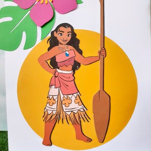 May include: A paper craft of Moana, a Disney princess, standing on a yellow circle with a brown paddle. She is wearing a pink and orange skirt with a brown grass skirt underneath. She has brown hair and brown eyes. The background is white with a green leaf and a pink flower.