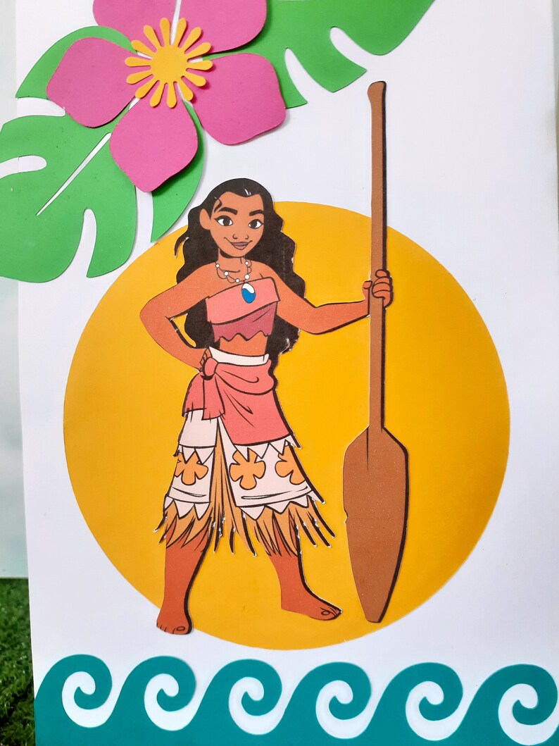 May include: A paper craft of Moana, a Disney princess, standing on a yellow circle with a brown paddle. She is wearing a pink and orange skirt with a brown grass skirt underneath. She has brown hair and brown eyes. The background is white with a green leaf and a pink flower.