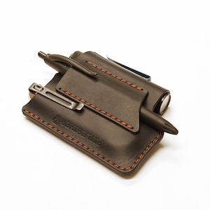 May include: A black leather carrying case with brown stitching. The case has two slots for pens and a small pocket for a torch. The case has the text "The Frontier" embossed on the front.