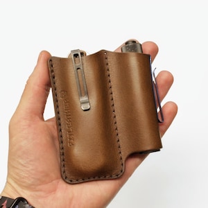 May include: A brown leather carrying case with a stitched design and a metal clip. The case has the text "FTL Leather" embossed on the front.