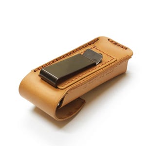 May include: A tan leather phone case with a metal clip. The case has a stitched edge and is designed to fit a smartphone.