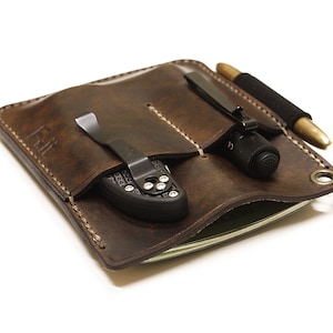 May include: A brown leather pocket organizer with three pockets. The organizer has a pen, a flashlight, and a small knife inside.