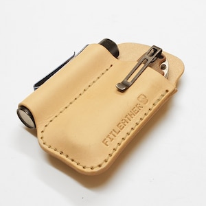 May include: A light brown leather pouch with a stitched edge and the text "FITTLEATHER CO." embossed on the front. The pouch is designed to hold a small flashlight and a pocket knife.