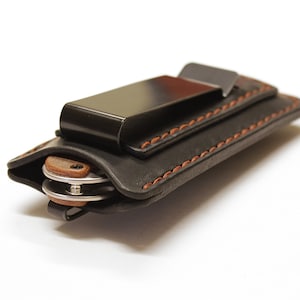 以下が含まれることがあります： 茶色のステッチと金属製のベルトクリップが付いた黒い革のナイフシース。シースは折りたたみナイフを入れるように設計されています。