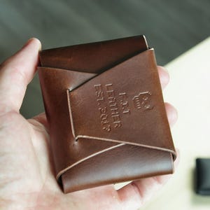 Peut inclure: Un portefeuille en cuir marron avec le texte "FAT LEATHER EST. 2014" en relief sur le devant.