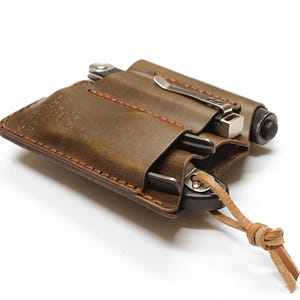 Peut inclure: Pochette en cuir marron pour multi-outils avec une sangle en cuir marron. La pochette comporte trois fentes pour outils et un porte-stylo. La pochette est fabriquée en cuir de haute qualité et est conçue pour être durable et résistante.